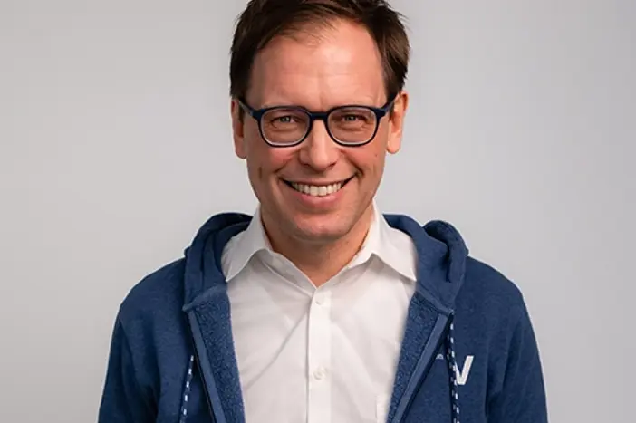 Franz Zöchbauer, Geschäftsführer von VerbundX, lächelt freundlich in einer blauen Sweatjacke über einem weißen Hemd. Der Hintergrund ist einfarbig.